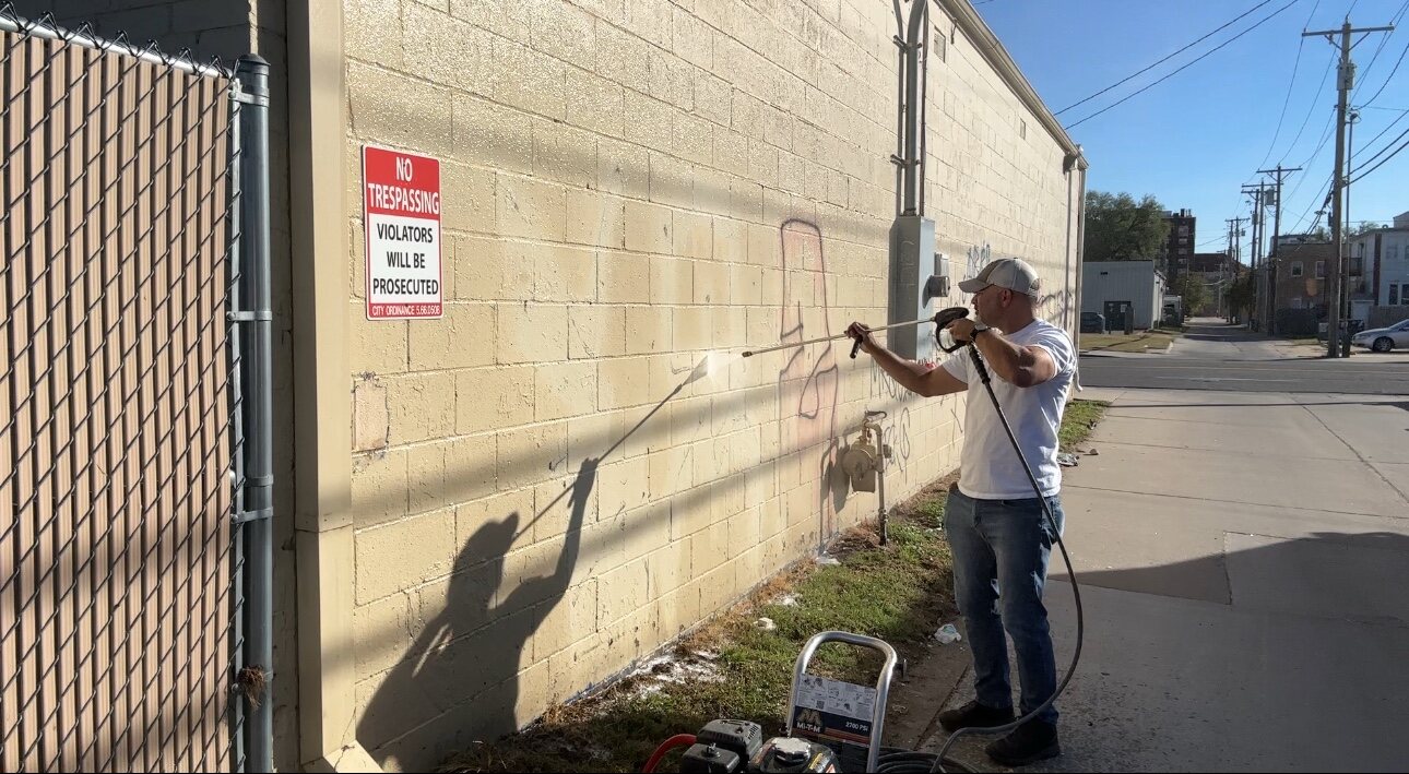 Buffalo Pressure Washing technician treating graffiti on a concrete block wall in Wichita