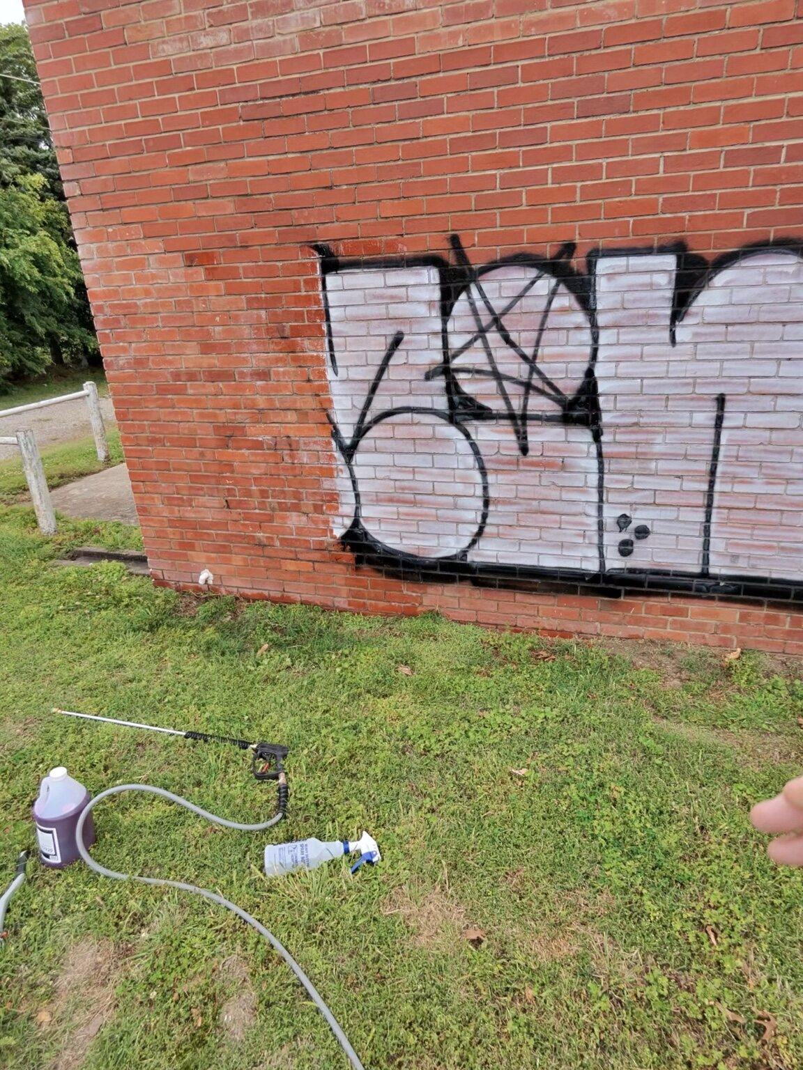 Graffiti-removal equipment positioned beside the tagged brick wall